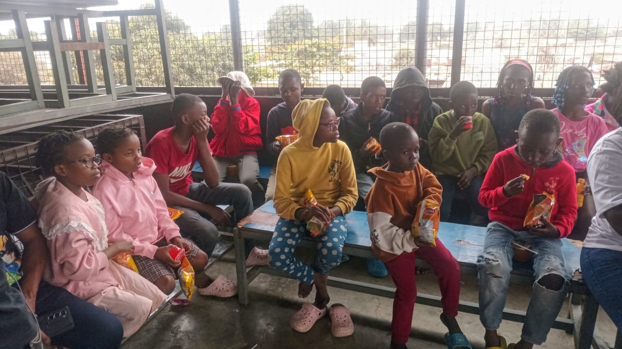 Children gathered around benches sharing refreshments at an outreach event