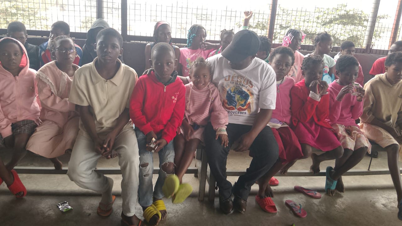 Children seated together on benches enjoying snacks at an outreach event