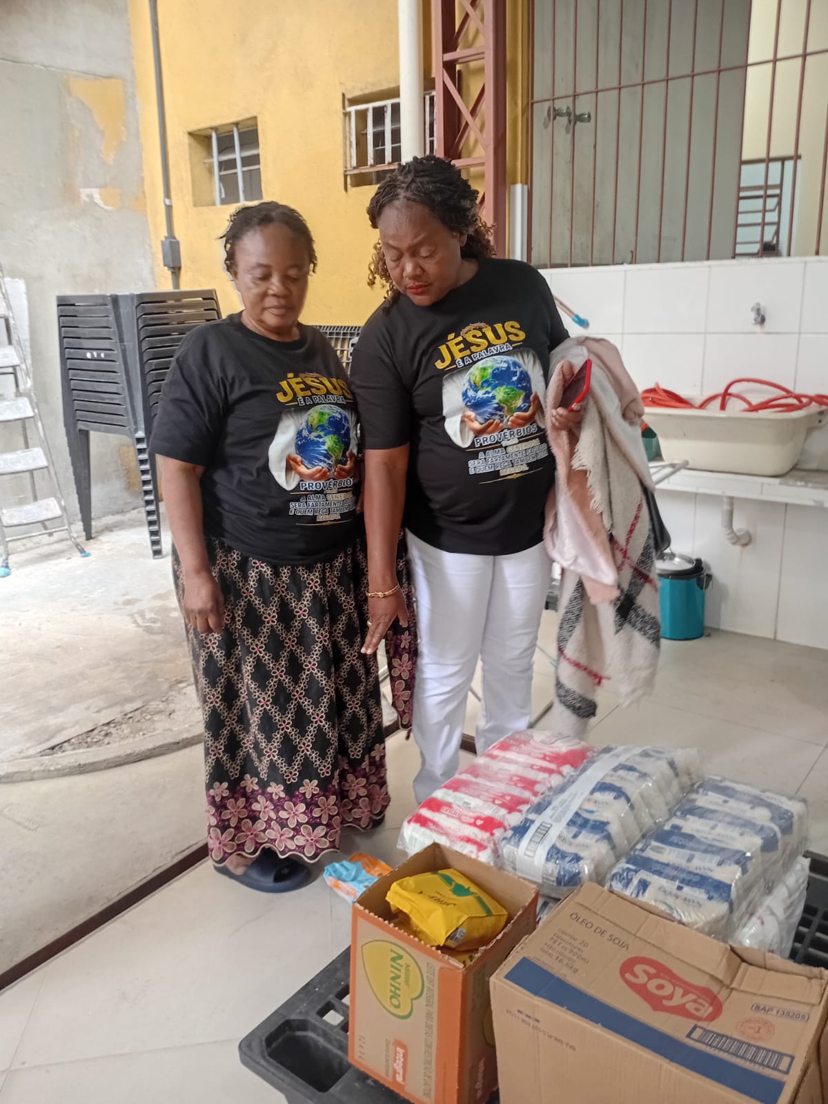 Two volunteers in Jesus é a Palavra shirts praying over donated food parcels