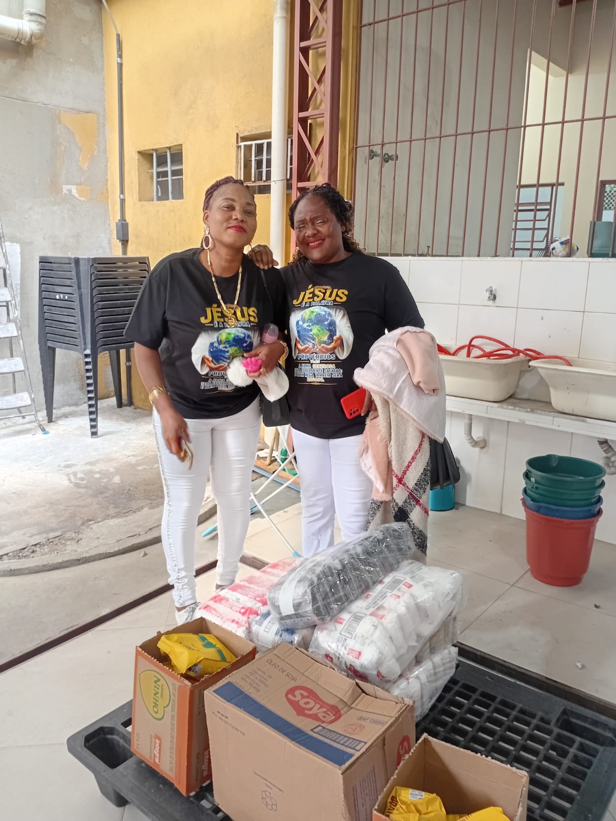 Two team members standing beside boxes of rice, oil and staple food donations