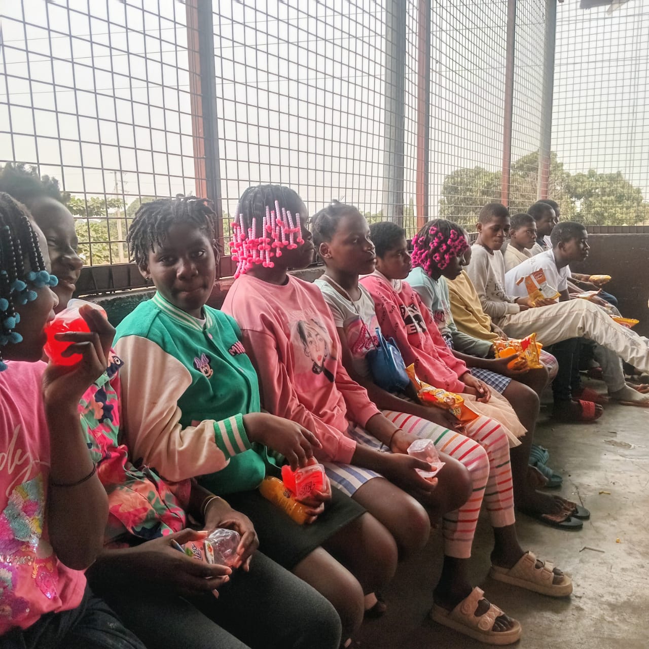 A row of children sitting together with snacks after a food distribution